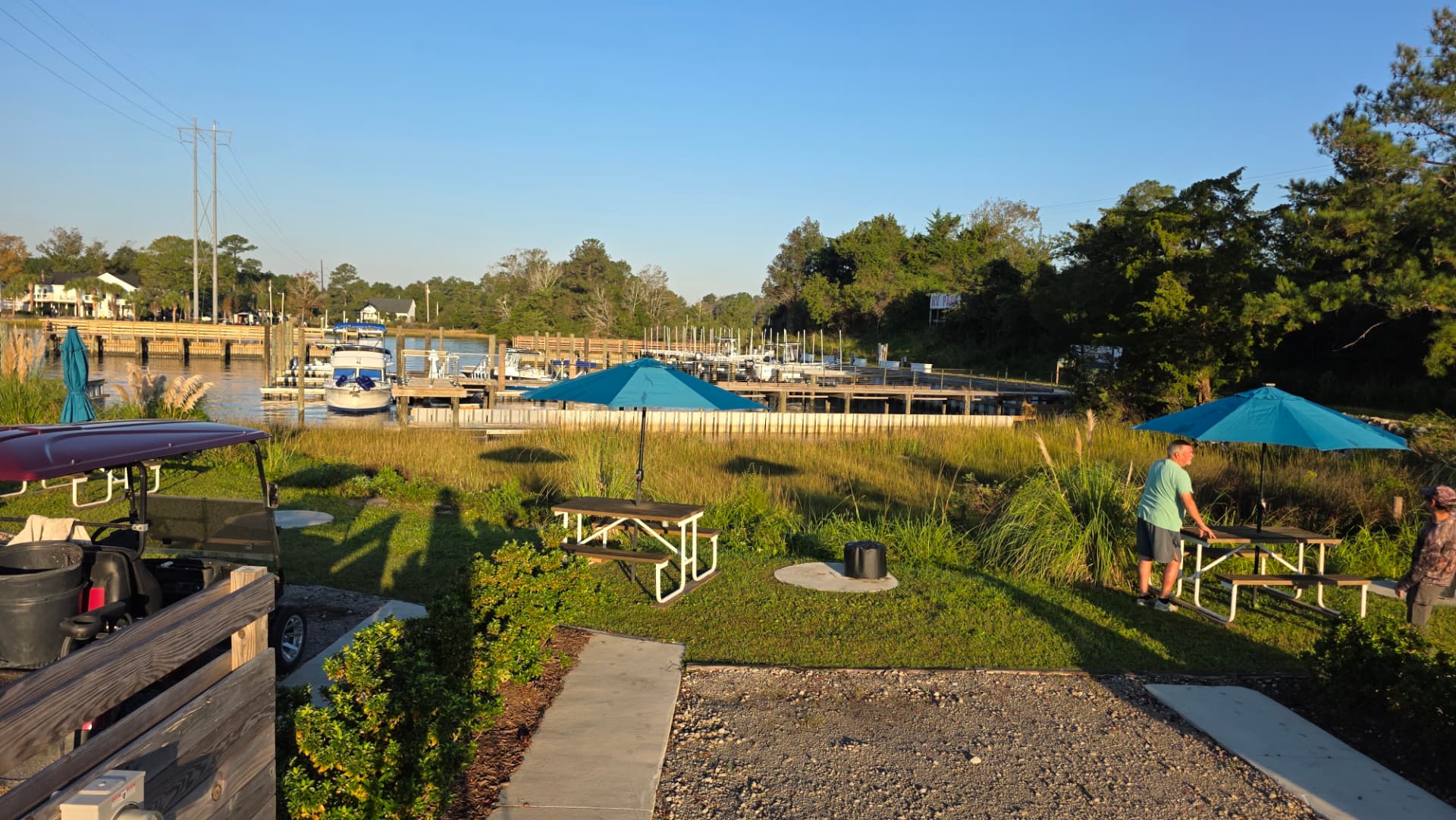 Marina-front green space with picnic tables and blue umbrellas at Core Creek