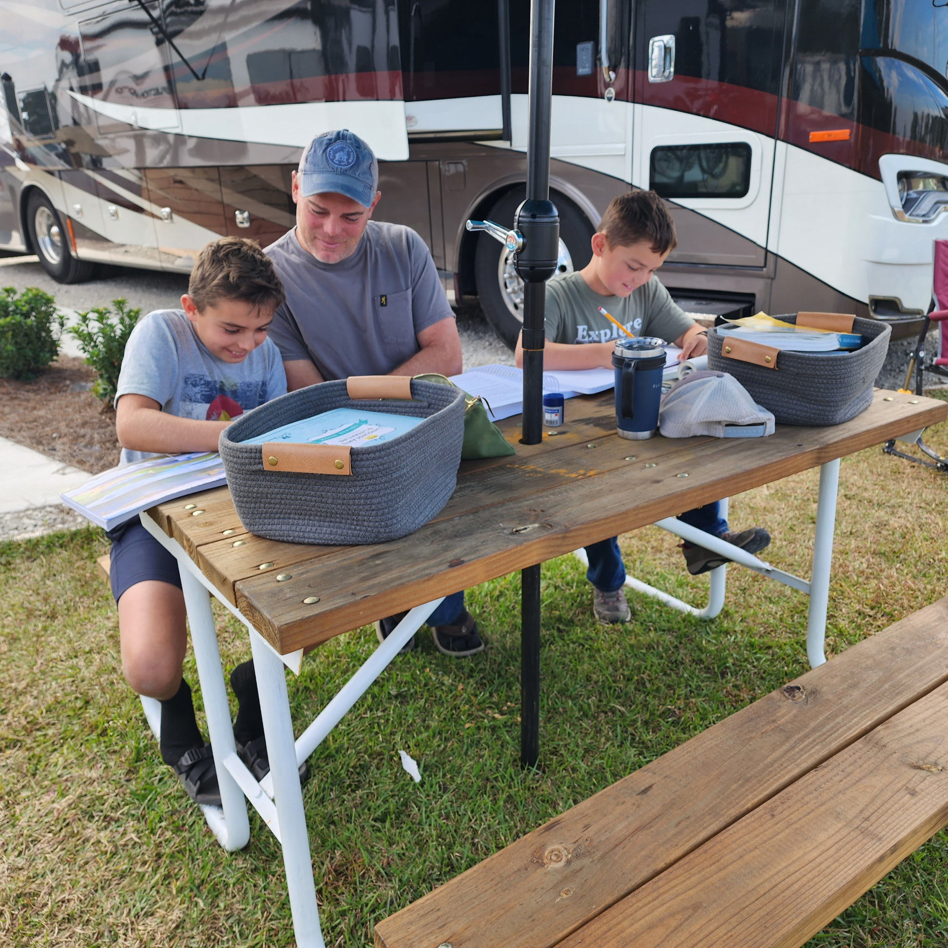 A parent and two children doing schoolwork at the picnic table at Core Creek site CCR4-116