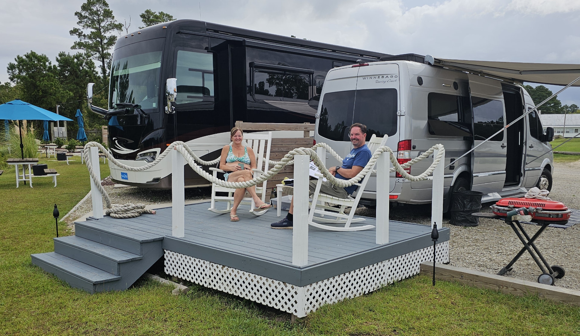 Guests relaxing in rocking chairs on the private deck at Core Creek site CCR4-116, with their motorhome and camper van parked beside it